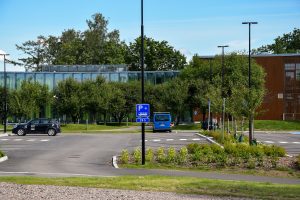 Pysäköintialue, jossa kolme autoa ja monta tyhjää paikkaa. Liikennemerkki liityntäpysäköinnistä.