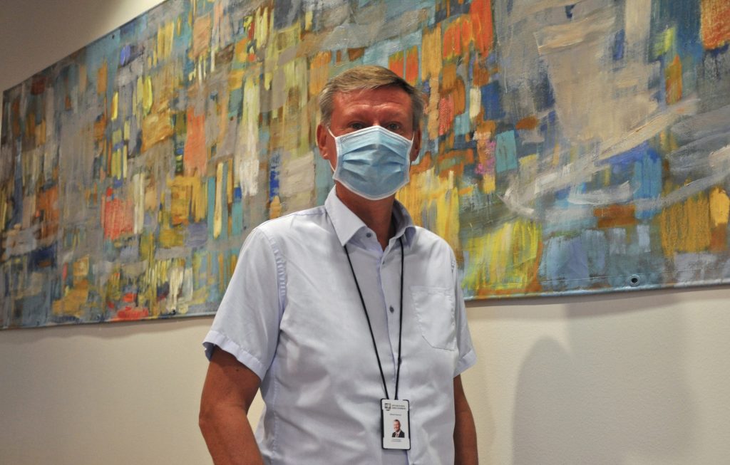 Kommundirektör Mikael Grannas Grannas bär ansiktsmask och han står framför ett konstverk som hänger på väggen. 