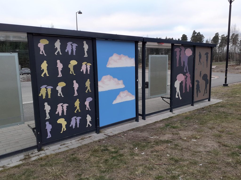 Busshållplatsen på baksidan, konstverk av eleverna i Sipoonlahden koulu på plywoodväggarna,. Människor med ett paraply och moln på en blå bakgrund.