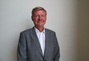 Mikael Grannas in a gray jacket in front of a white wall.