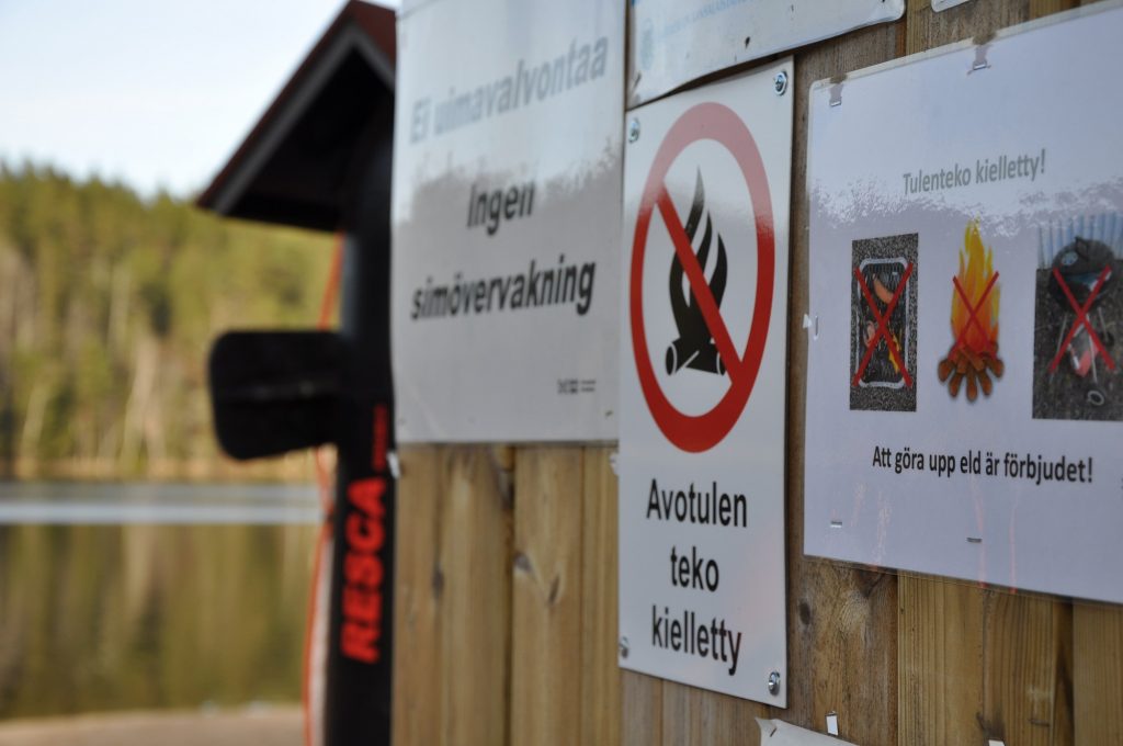 Information på en anslagstavla vid badstrand. Text: "Att göra upp eld är förbjudet".