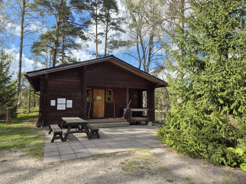 Ruskea saunarakennus, jonka edessä pihapöytäryhmä ja vieressä suuri kuusi