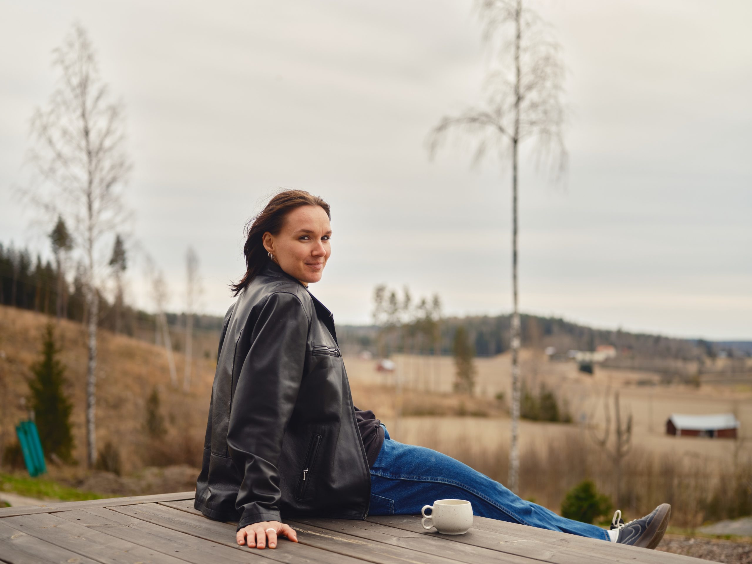 Senni Salminen istuu terassilla ja hymyilee. Taustalla näkyy kaunis peltomaisema.