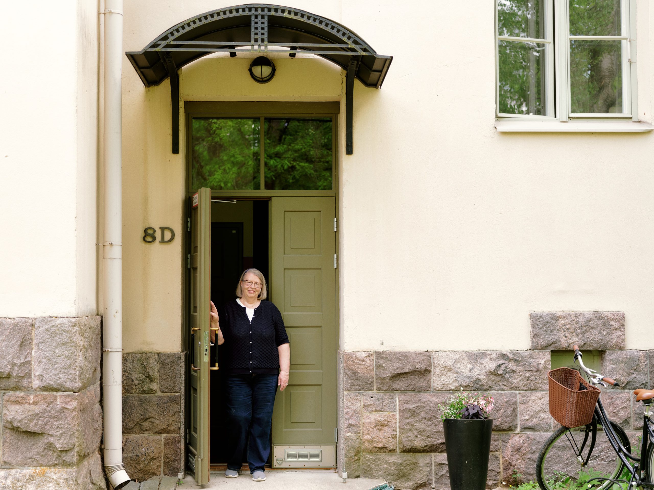 Riitta Nissinen står vid nedre dörren till det gamla jugendhuset och håller dörren öppen.