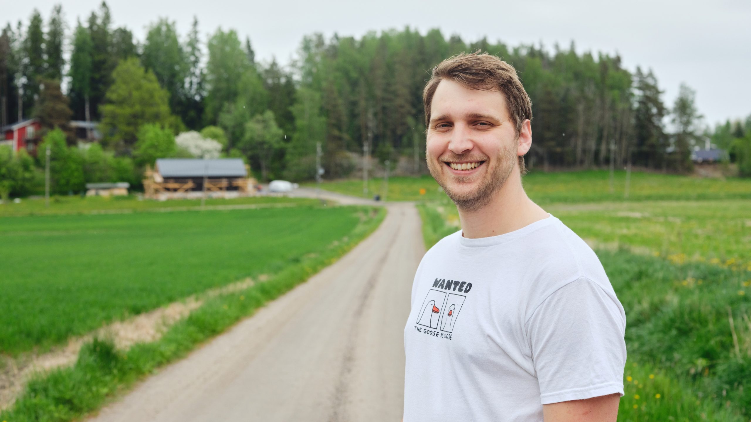 Marius Van der Busse står leende på en grusväg som leder till hans hem.
