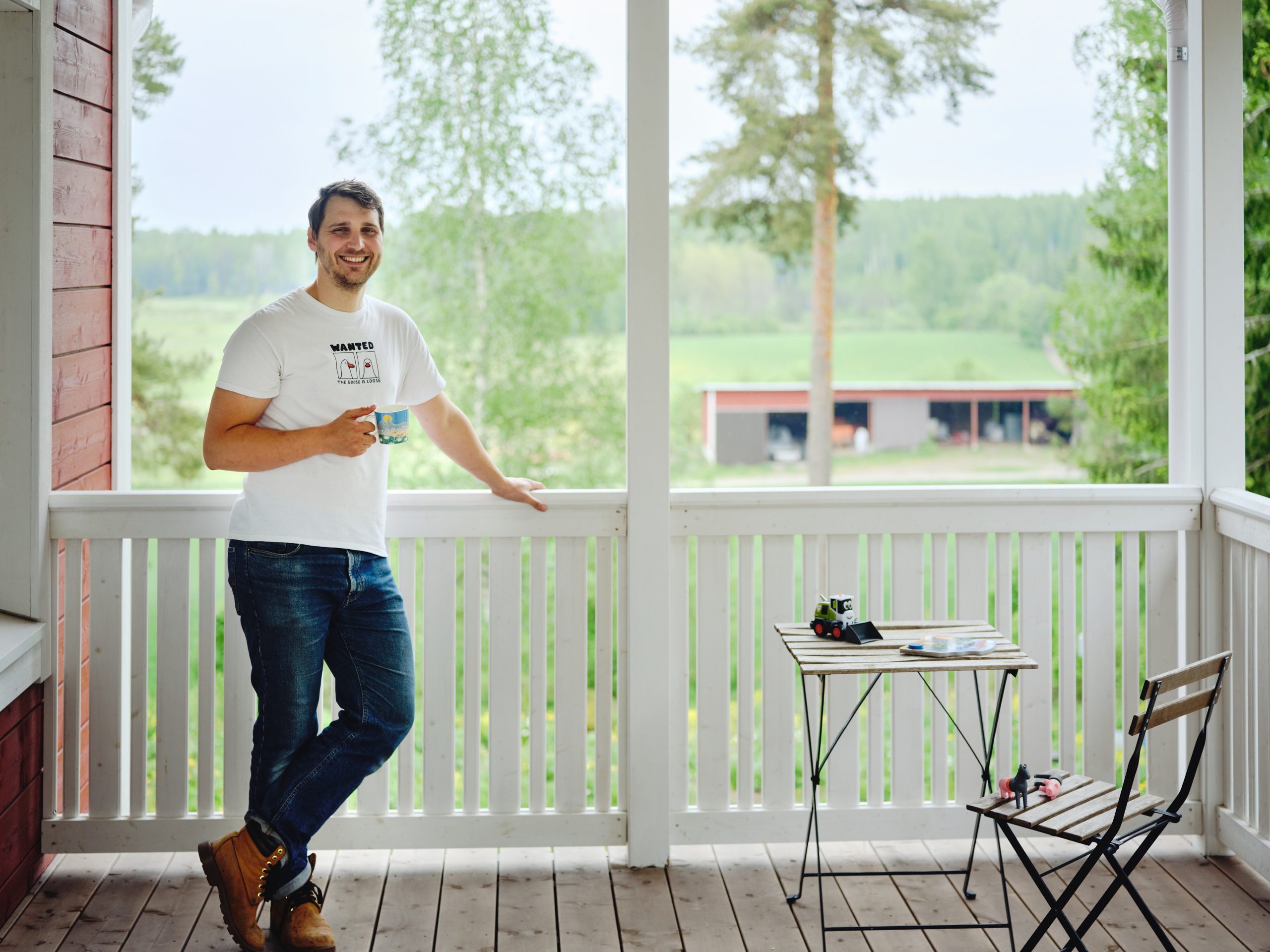 Marius Van der Busse seisoo kahvikuppi kädessään kotinsa parvekkeella. Taustalla näkyy kaunis pelto- ja metsämaisema.