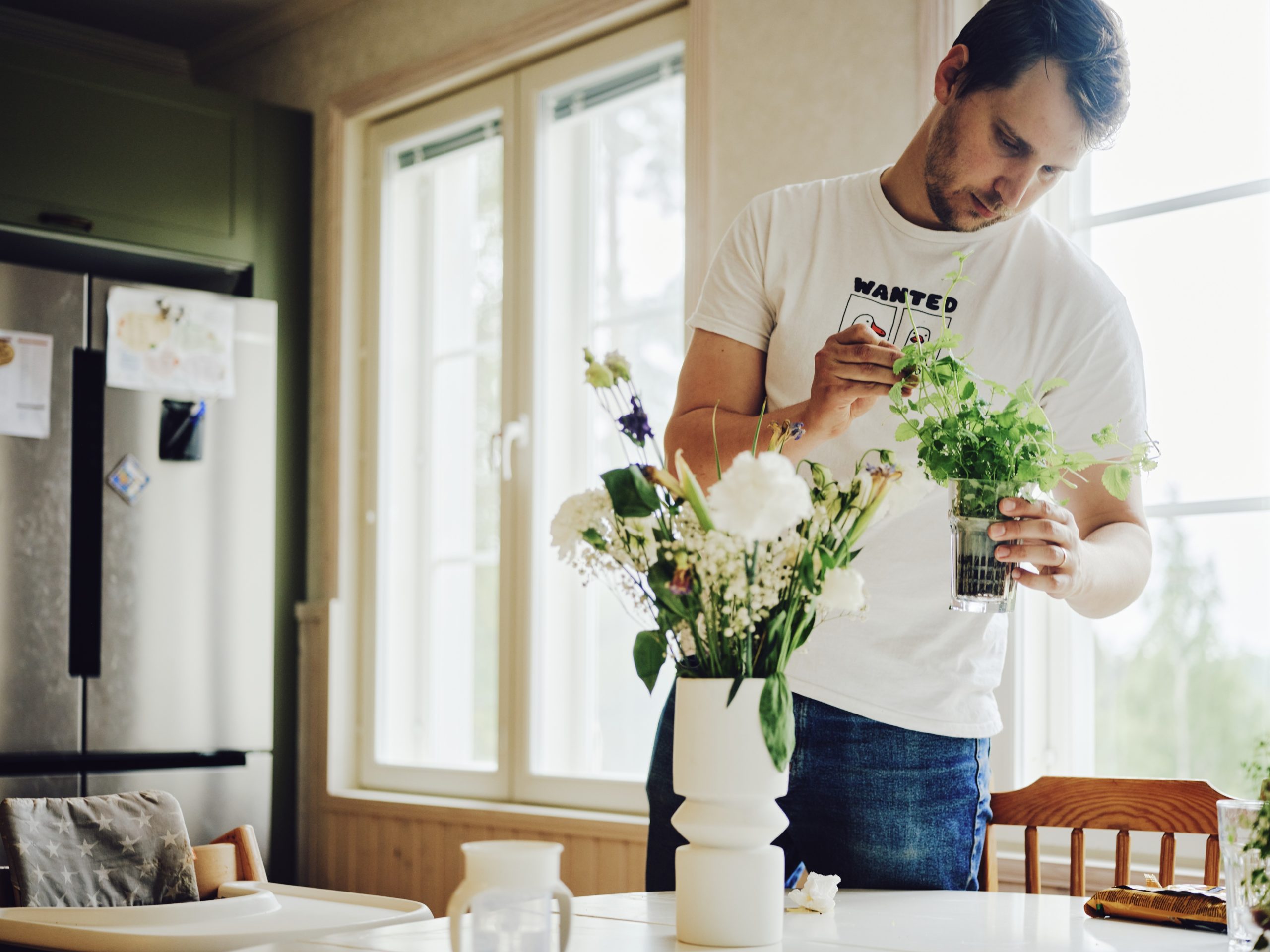 Marius Van der Busse asettelee keittiössä yrttejä maljakkoon. Edessä pöydällä on kukkia maljakossa.