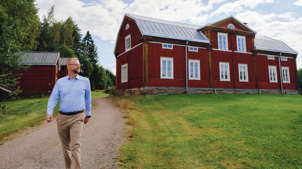 Jari Vesanen kävelee Varpulan hirsitalon edustalla.